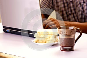 Coffee mug, stack of bread and man working on a laptop computer in the background