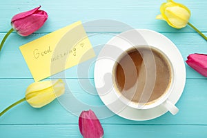 Coffee mug with tulip flowers and notes good morning on blue background, breakfast on Mothers day or Womens day