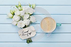 Coffee mug with white flowers and notes good morning on blue rustic table from above. Beautiful breakfast. Flat lay.