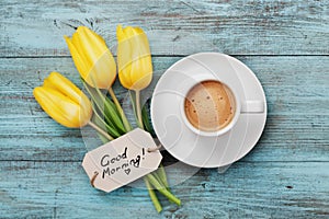 Coffee mug with yellow tulip flowers and notes good morning on blue rustic table from above