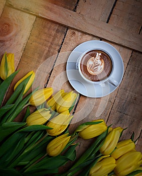 Coffee mug with yellow tulip flowers and notes good morning on blue rustic table from above, breakfast on Mothers or Women day