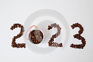 Coffee New Year 2023 concept. Number made of coffee beans. A cup filled with coffee beans as a Christmas ball. On white