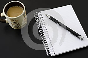Coffee, notebook and pen on black wooden table.