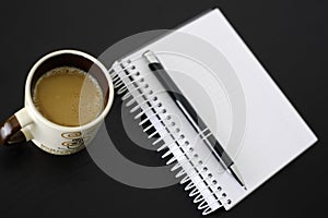 Coffee, notebook and pen on black wooden table.