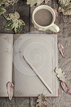 Coffee and notebook on wooden table decorated with autumn leaves