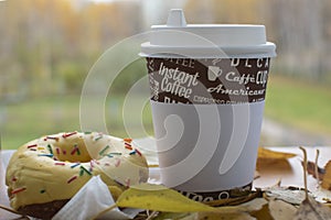 Coffee in a paper cup and a donut on a table in fallen foliage