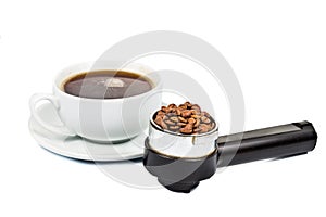 Coffee portafilter filled with coffee beans with a cup of freshly brewed espresso at the background