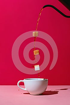 Coffee poured from black pot in a white cup with three levitating sugar cubes on red