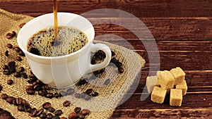 Coffee is poured into a white cup on the table on him located coffee beans, burlap tablecloth and brown sugar cubes on
