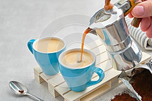 Coffee pouring in  cups from Italian coffee espresso maker. Two coffee mugs and moka coffee pot