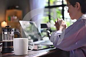 A coffee press and a cup on a work desk with a person working from home