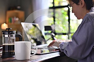 A coffee press and a cup on a work desk with a person working from home