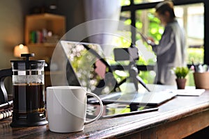A coffee press and a cup on a work desk with a person working from home