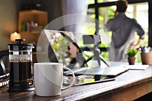 A coffee press and a cup on a work desk with a person working from home