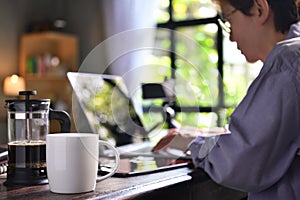 A coffee press and a cup on a work desk with a person working from home photo