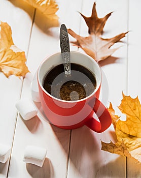 Coffee in a red cup, marshmallows and yellow leaves. Cozy time with a cup of coffee in the autumn season
