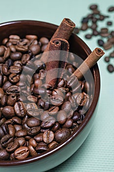 Coffee roasted beans with cinnamon sticks, star anise in brown ceramic mug on blue background half view vertical macro