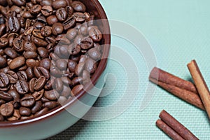 Coffee roasted beans with cinnamon sticks, star anise in brown ceramic mug on blue background quarter view horizontal macro