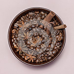 Coffee roasted beans with cinnamon sticks, star anise in brown ceramic mug on pink background square macro