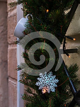 Coffee roasters shop in downtown with winter decor. Green natural fir tree branch with white cup lights on cafe facade