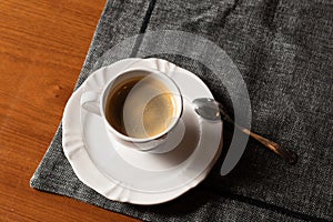 Coffee served on white crockery, with a small spoon over a dark placemat. With space for text.