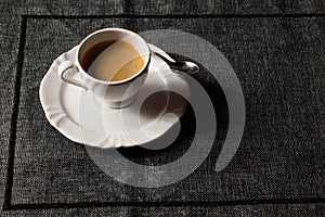 Coffee served on white crockery, with a small spoon over a dark placemat. With space for text.