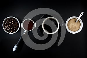 Coffee setting with beans, porta filter, coffee in a black cup and sugar