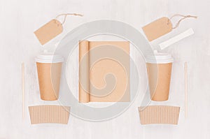 Coffee shop template for branding identity - two brown paper cups with blank notebook, label, sugar on white wood board, top view.