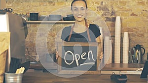 A coffee shop worker holds a Open sign.