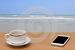 Coffee and smart phone on wooden table with tropical sea and beach