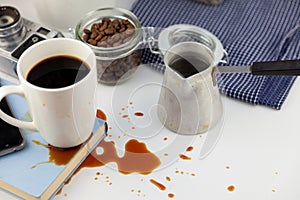 Coffee spilled on a book on the desktop. A cezve for coffee, coffee beans, a white cup of coffee, spill a drink on the table,