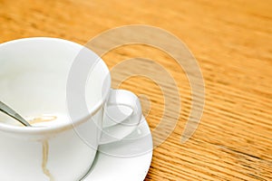 Coffee stain in white cup and coffee spoon with saucer on wooden table