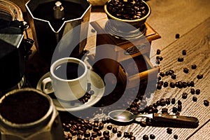 Coffee stuff. A white cup with black coffee, Italian coffee maker moka, a mill and grains over a wooden table. Rustic style