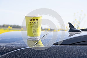 Coffee take-away in a paper cup in the car with text. is on the dirty roof of a black car