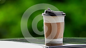 coffee takeaway in a paper cup on top of the car roof green tree background at sunrise in the morning,  selective focus, soft