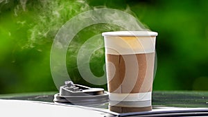 coffee takeaway in a paper cup on top of the car roof green tree background at sunrise in the morning,  selective focus, soft