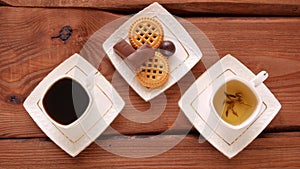 Coffee or tea choice. Steaming hot drinks cups with sweets on wooden table. Freshly brewed espresso and herbal mix with steam.