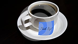 Coffee with text message - Think Big. With message sticked to a cup of black coffee on the table.