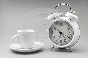 Coffee Time. Coffee cup and white alarm clock on a soft background