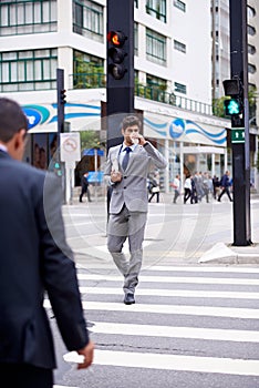 Coffee to go. A full length shot of a handsome young businessman walking across a city street.