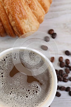 Coffee to go. Paper cup with tasty drink, croissant and beans on white wooden table, flat lay
