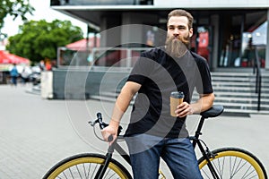 Coffee to go. Side view of young bearded man drinking coffee while sitting on his bicycle outdoors