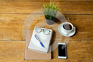 Coffee up and notebook, pen with glasses, cell phone on wooden table.