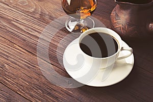 Coffee in white cup with cognac and clay cezve on wooden background. Copy space. Food background. Toned