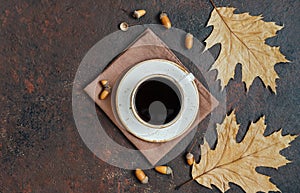 Coffee in a white cup with leaves and acorns on a brown background. Acorn coffee. Space for text. Top view, flat lay