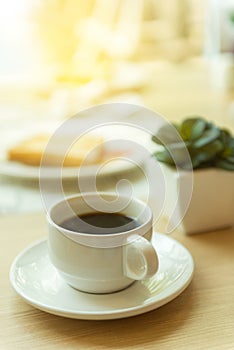 Coffee in white cup on wood table with morning sunlight