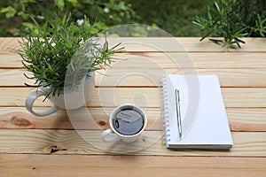 Coffee with white notebook and green plant on wooden table at exterior