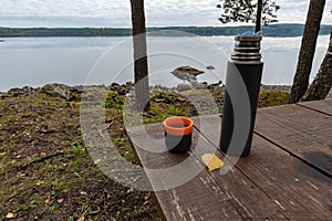 Coffeecup and a thermos at a table near a lake photo