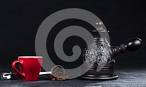 A coffeepot, cup and steel measuring spoon with coffee beans