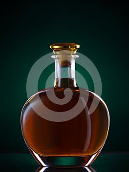 Cognac bottle of golden color on the table on dark green background